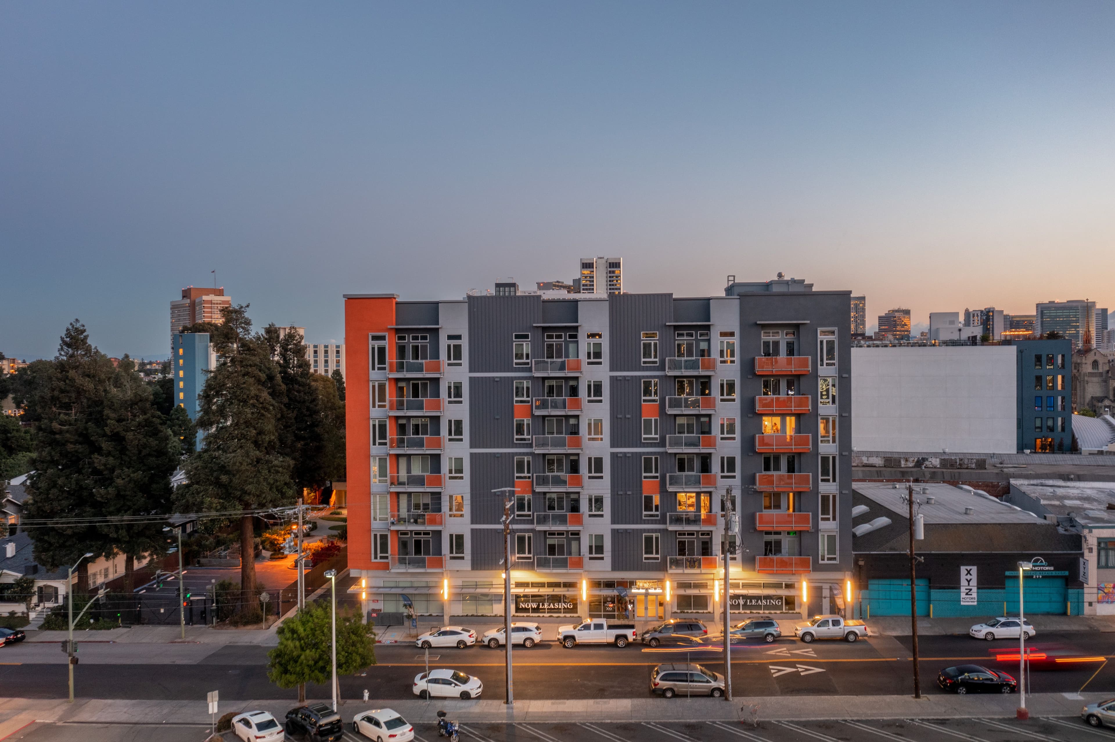 Edson House at dusk, a seven-story apartment building with grey and orange panels on a wide Oakland street