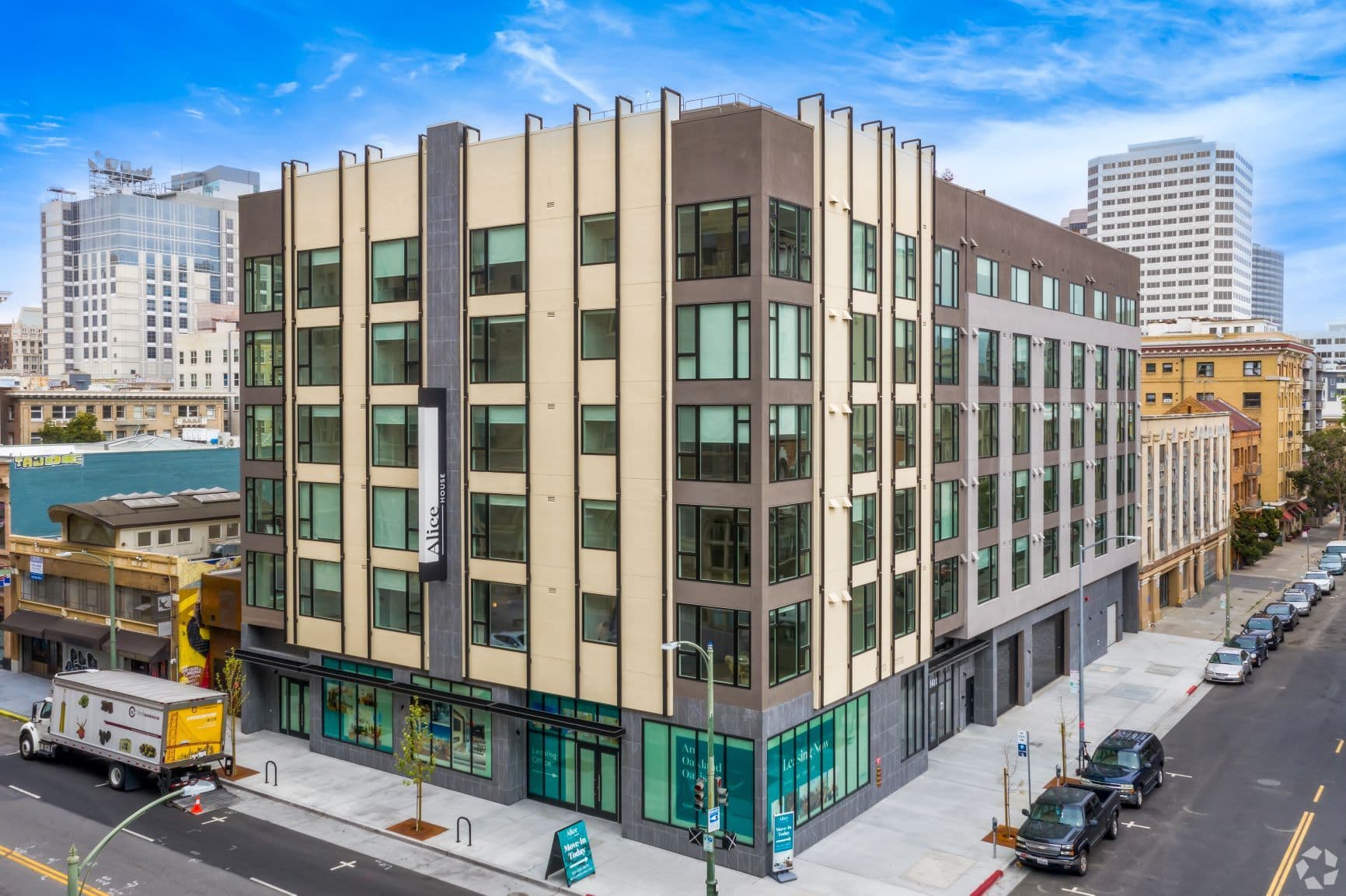 Alice House, a six-story building with tan and brick-red panels at a downtown Oakland corner, towers behind