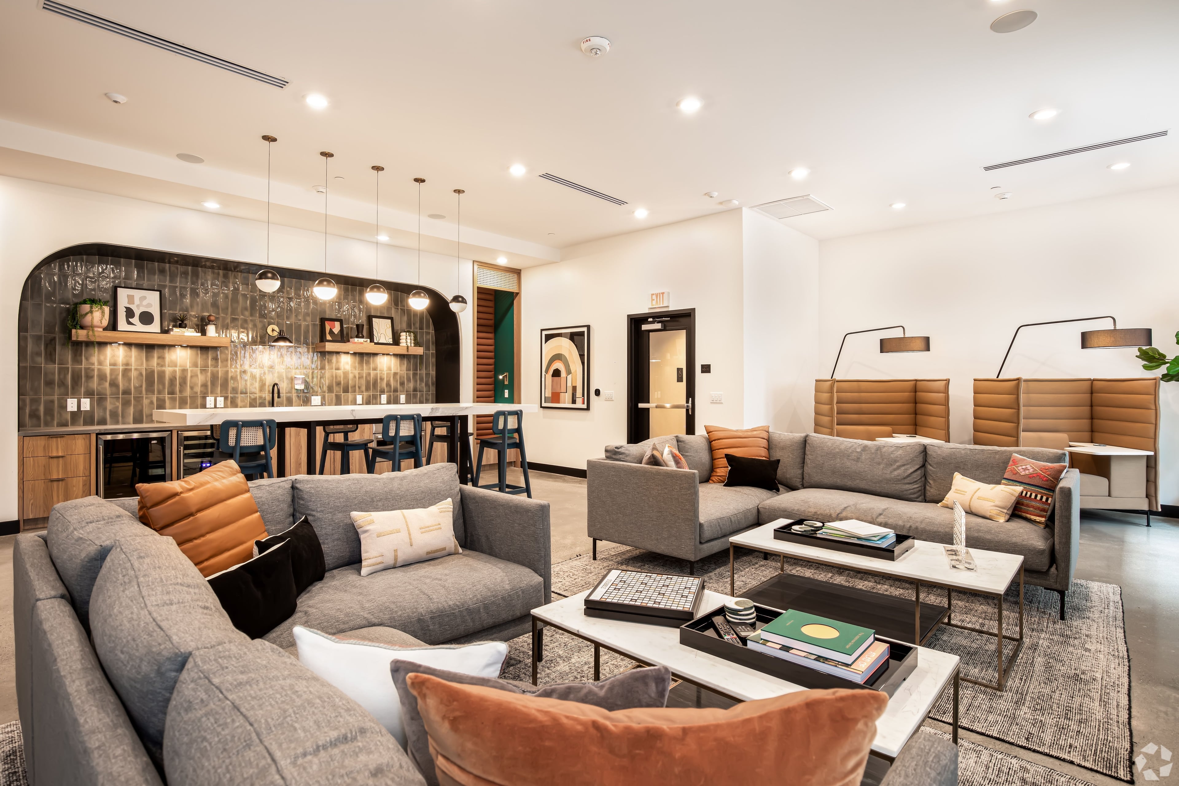 Resident lounge with a grey sectional, leather pillows, and a bar with pendant lights
