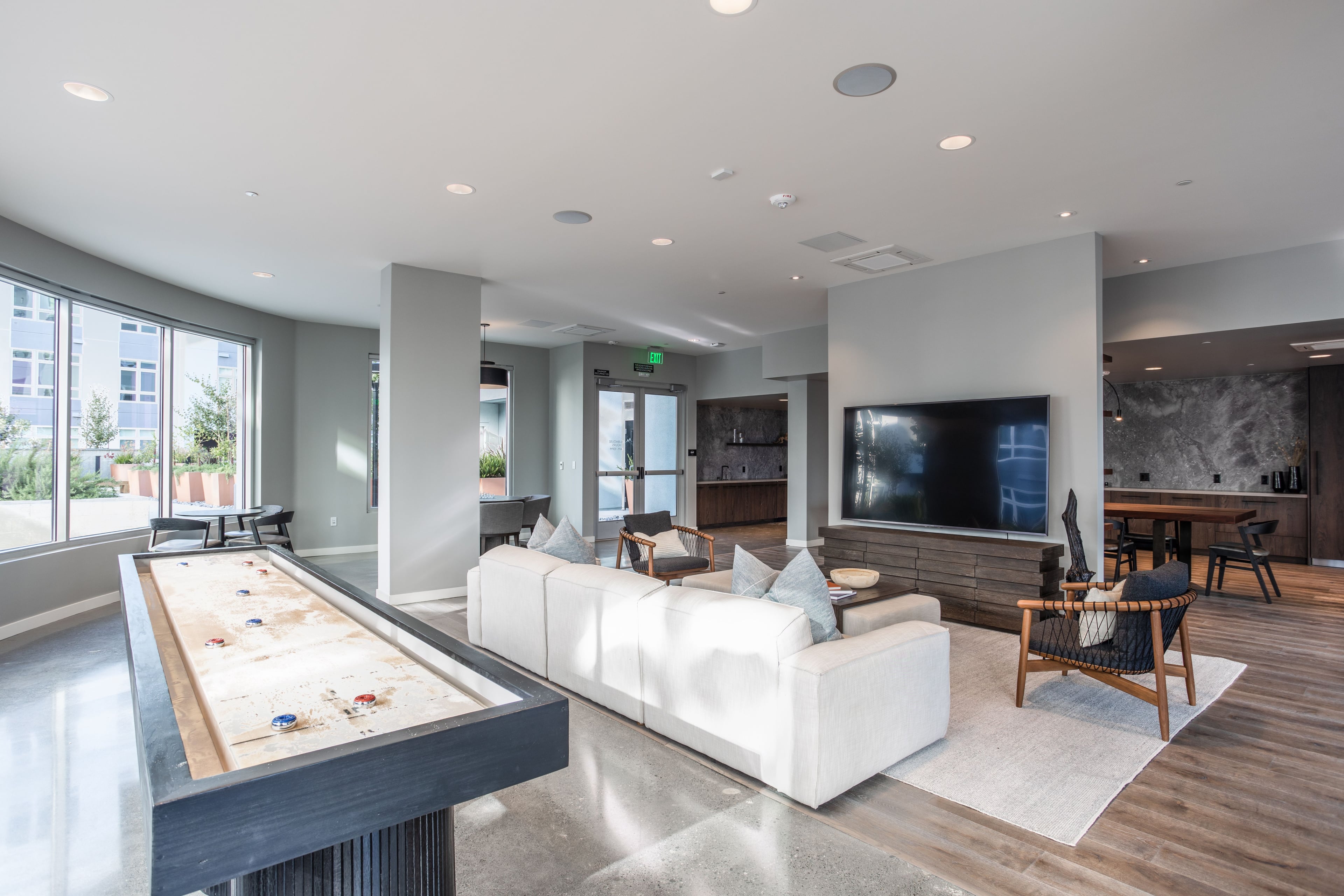 Clubroom with a shuffleboard table, white sofas, and a wall-mounted TV