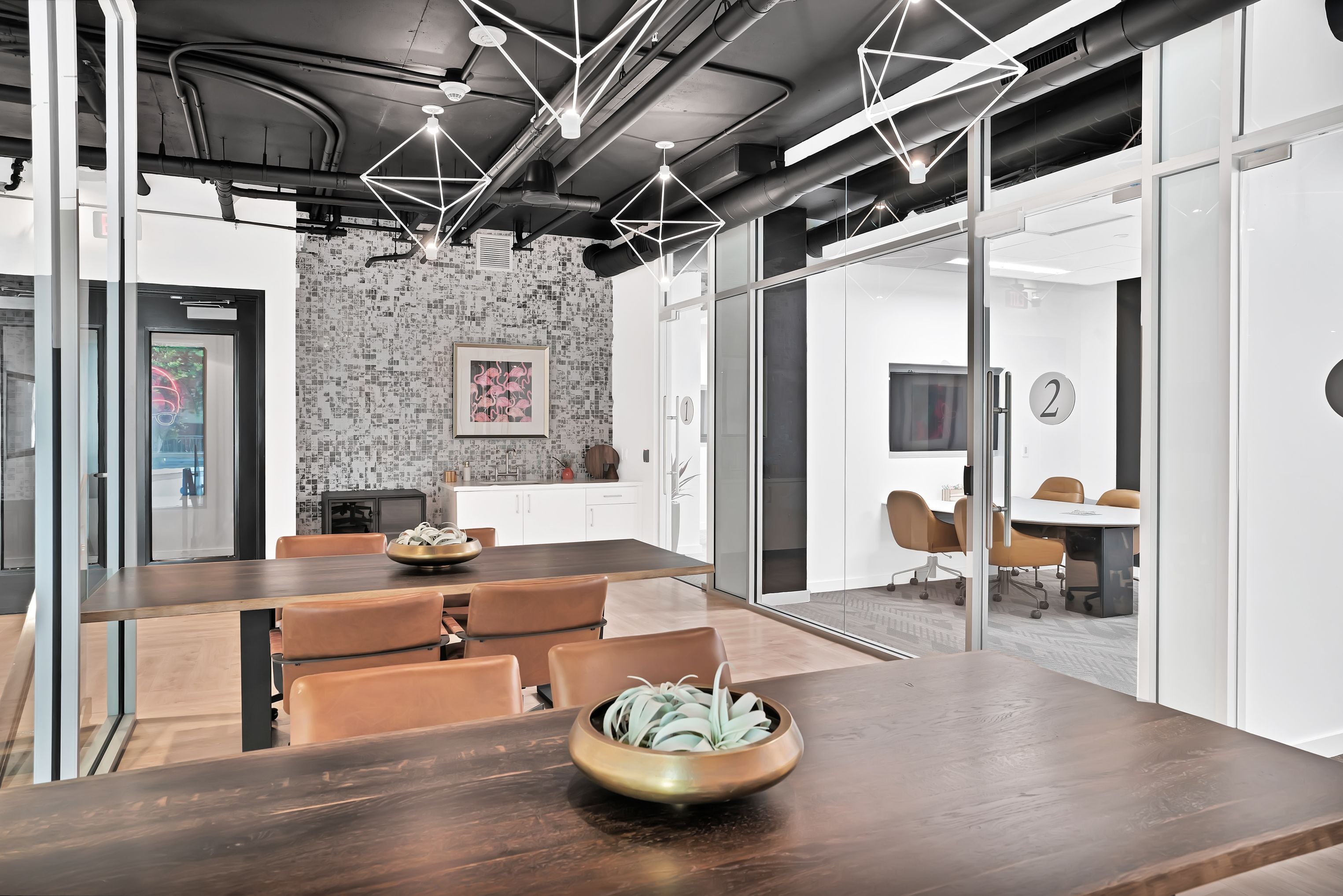 Co-working area with wood tables, leather chairs, and glass-walled meeting rooms