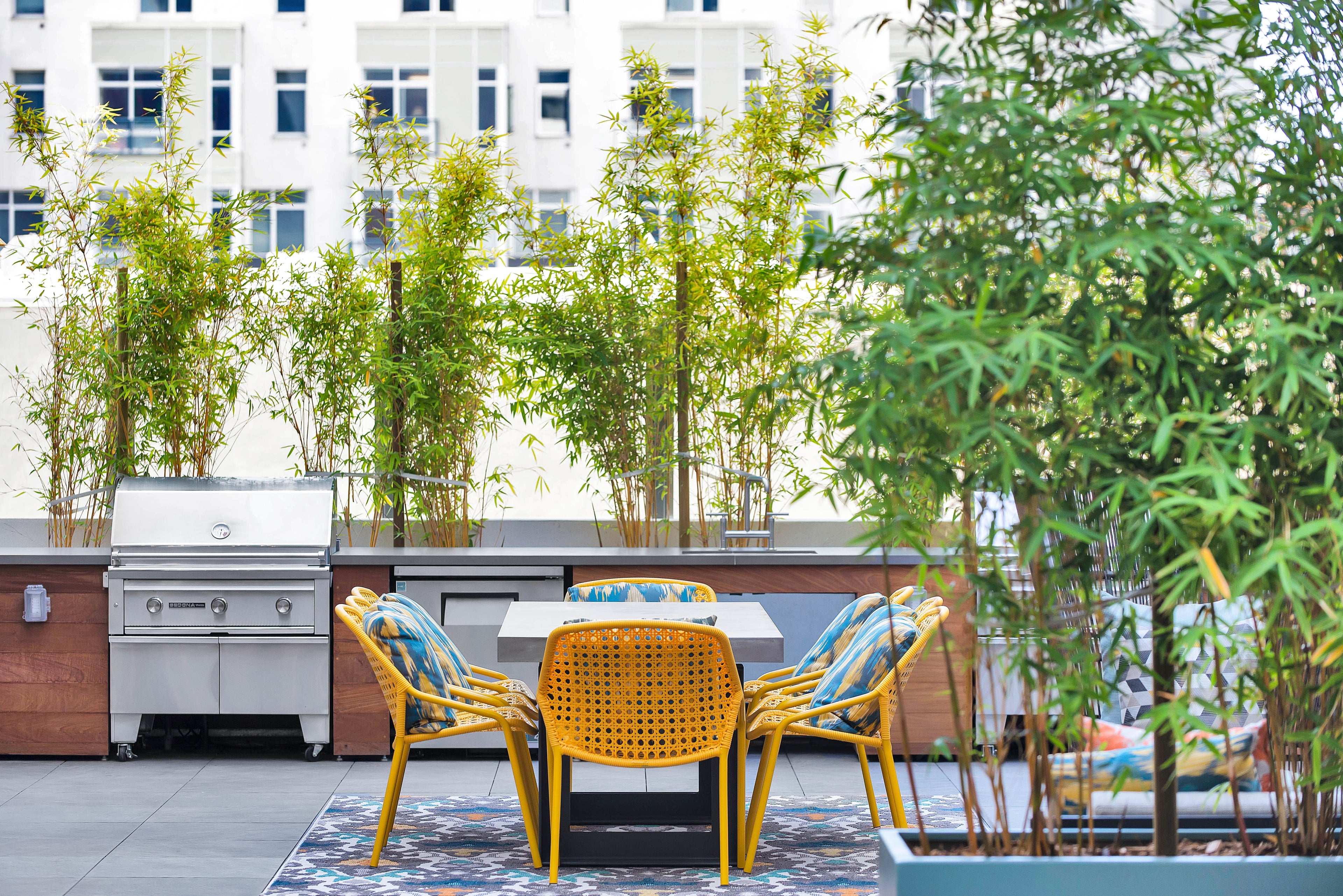Outdoor kitchen with a grill, bamboo planters, and yellow chairs