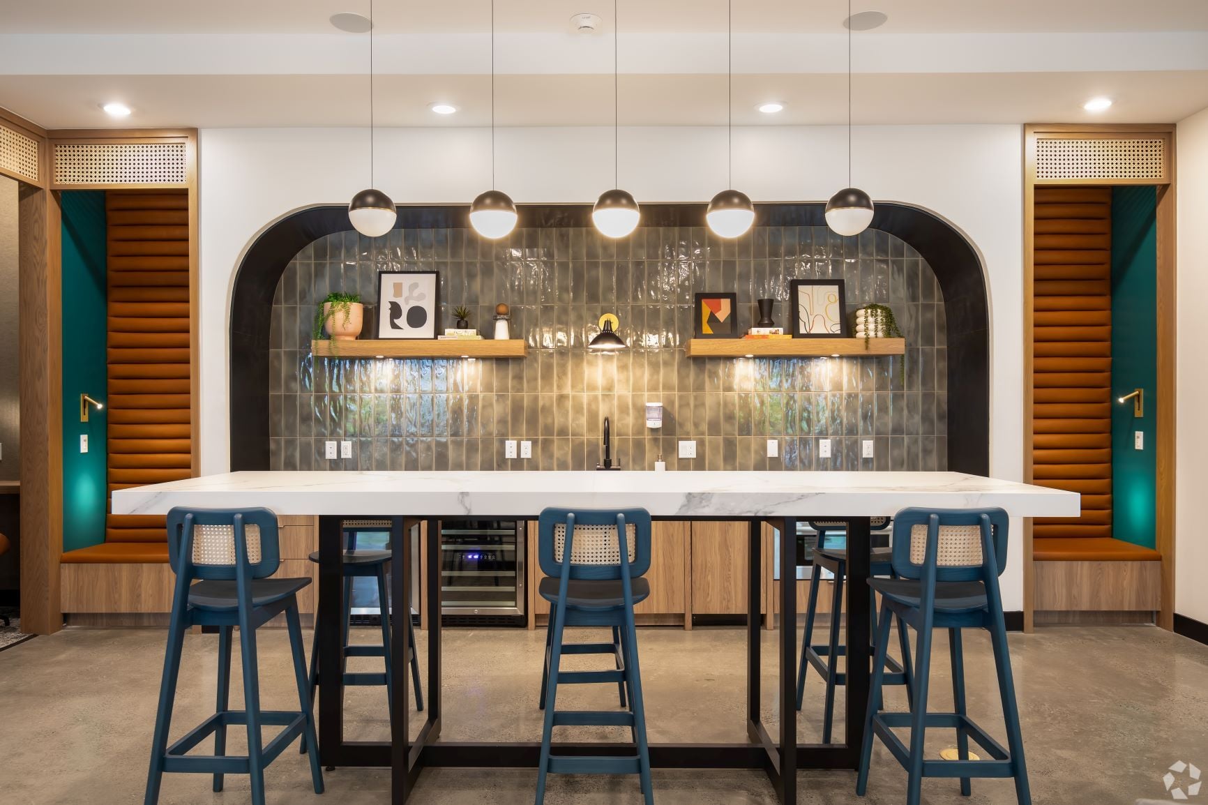 Bar with a marble island, blue stools, green tile, and open shelving under an arch