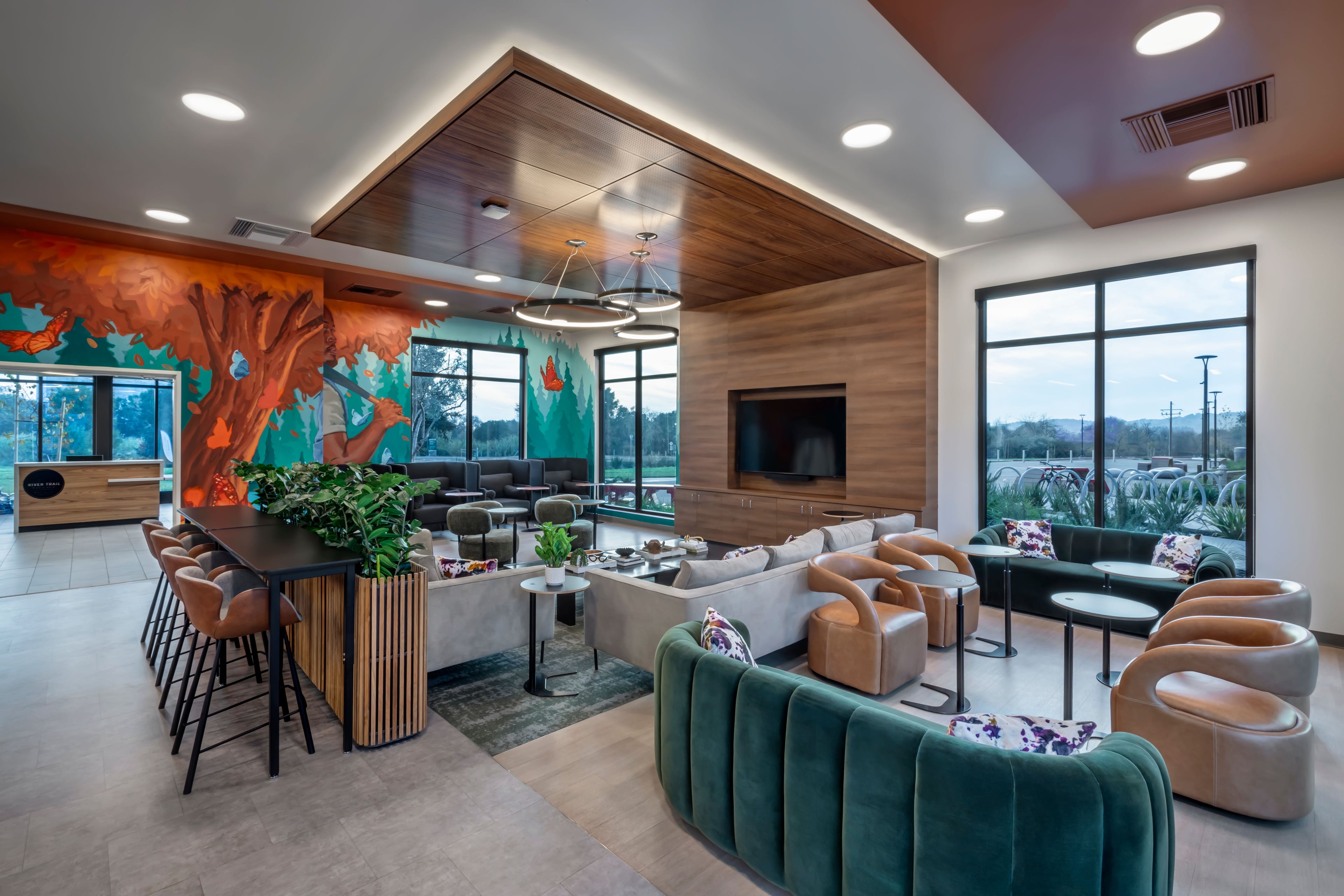 Clubroom with a green velvet sofa, blush armchairs, a wood-clad ceiling, and a large mural