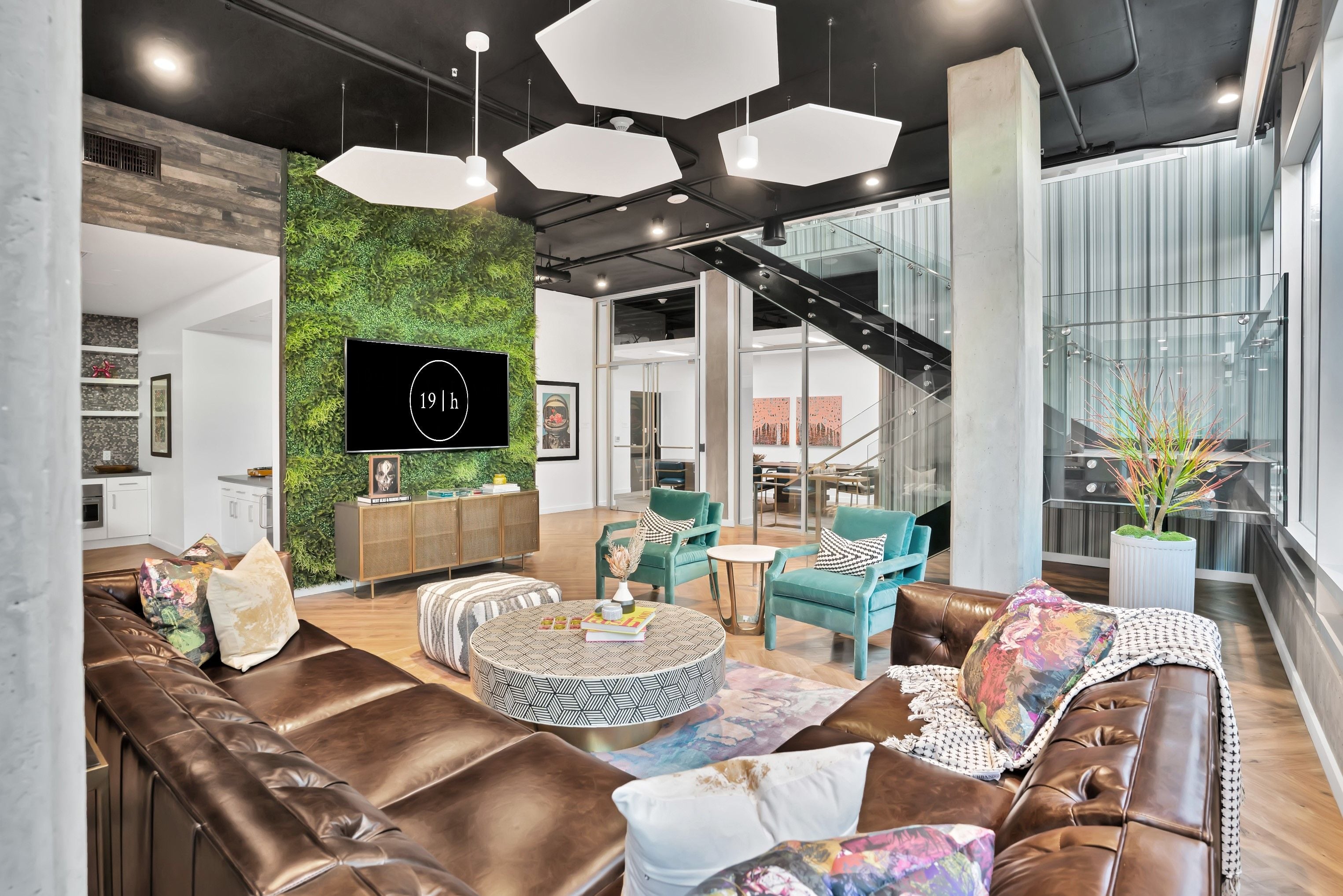 Resident lounge with brown leather sofas, a living green wall, hexagonal pendant lights, and a TV