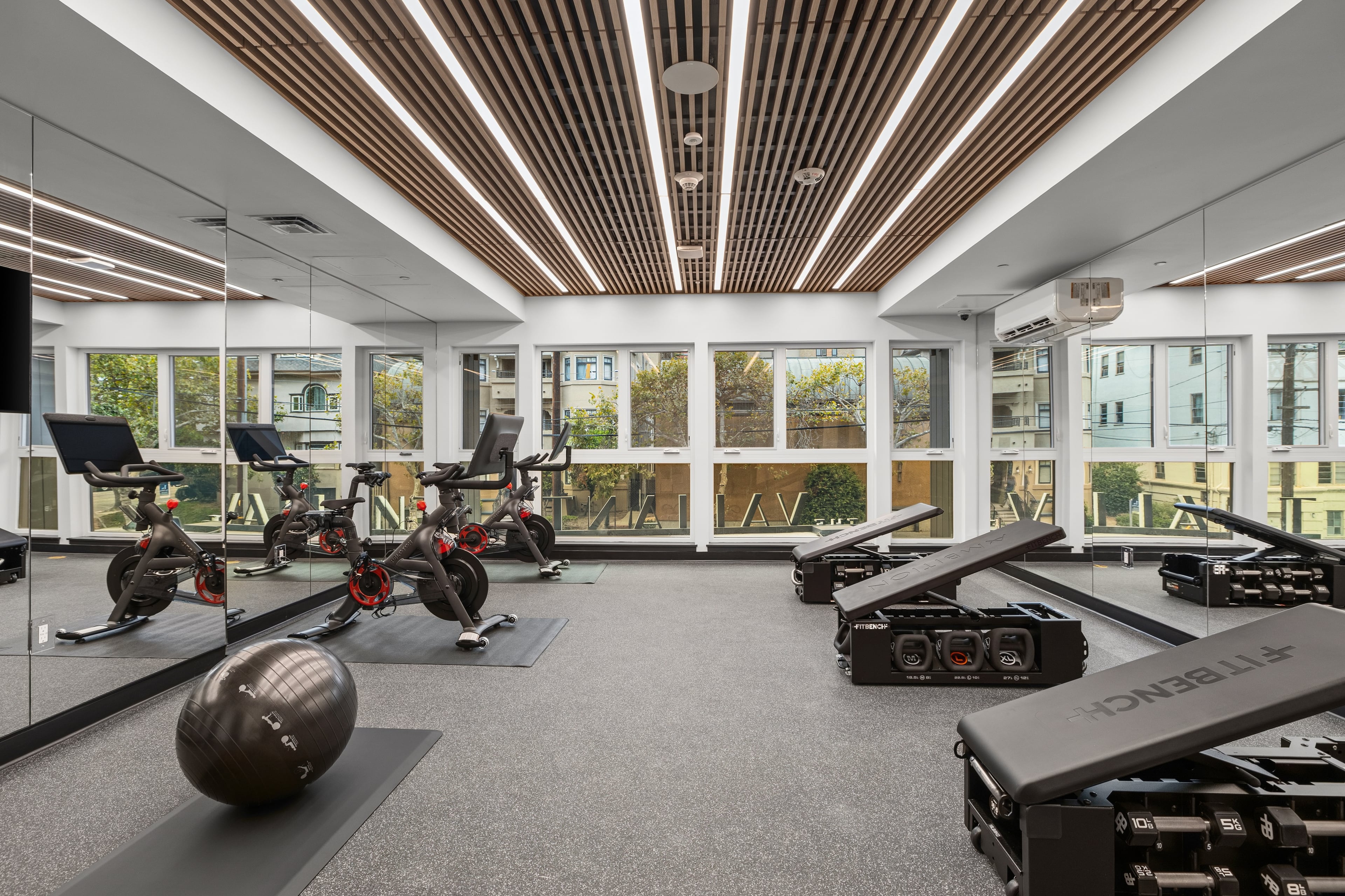 Fitness room with spin bikes, a slatted wood ceiling, and windows onto the street