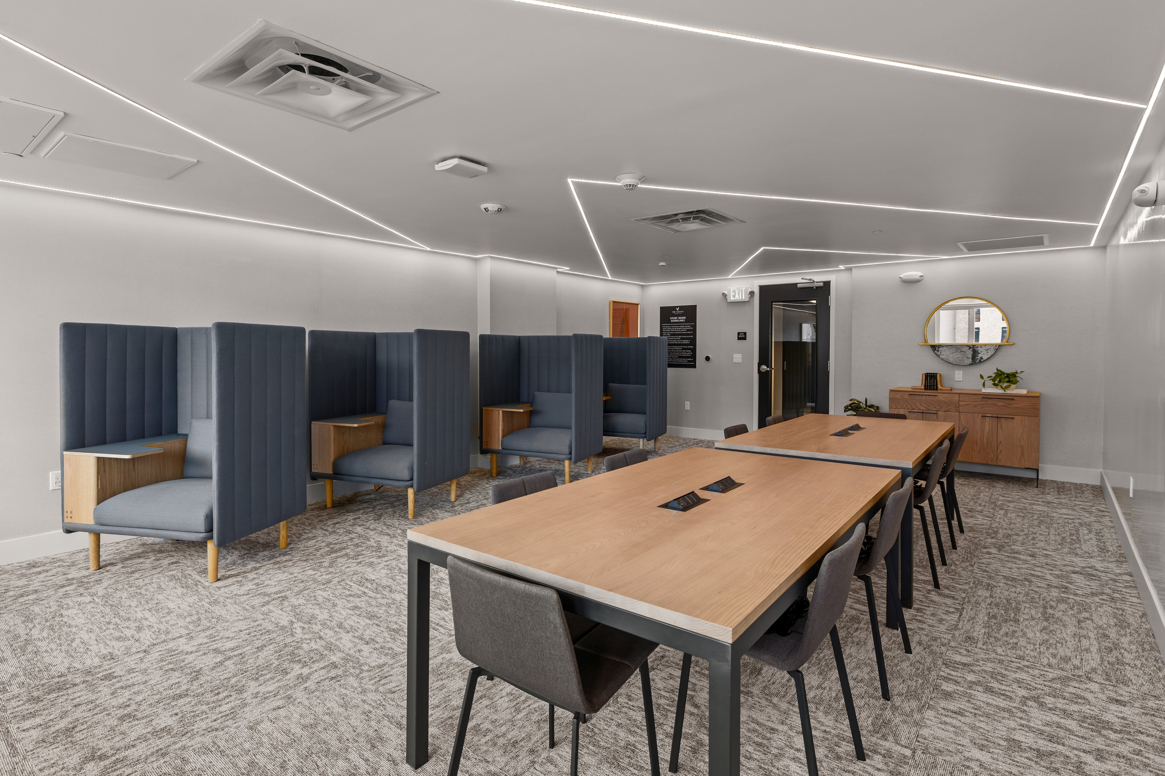 Study room with grey booths, a long wood table, and a lit ceiling pattern
