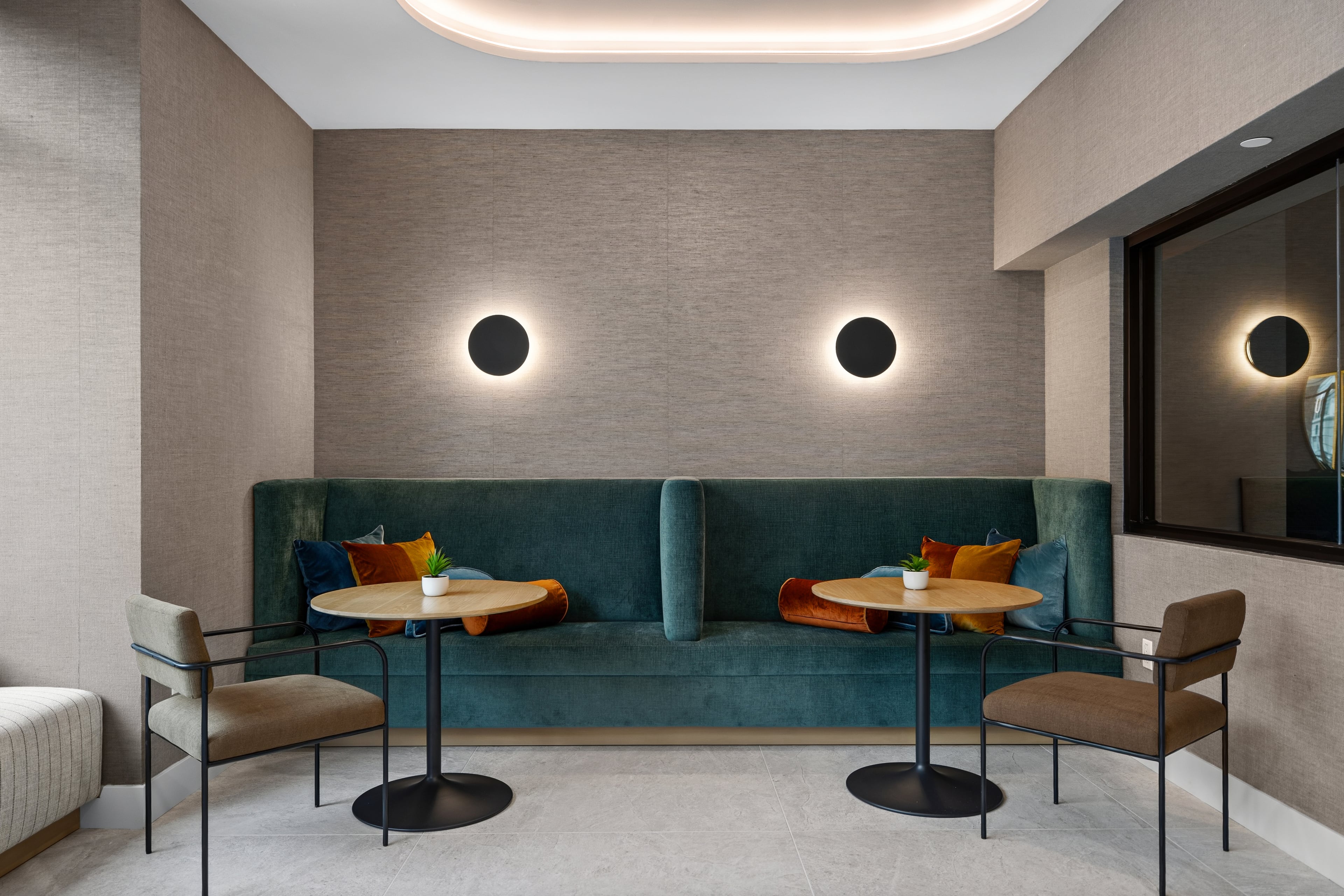 Lounge alcove with a green velvet banquette, small tables, and round wall lights