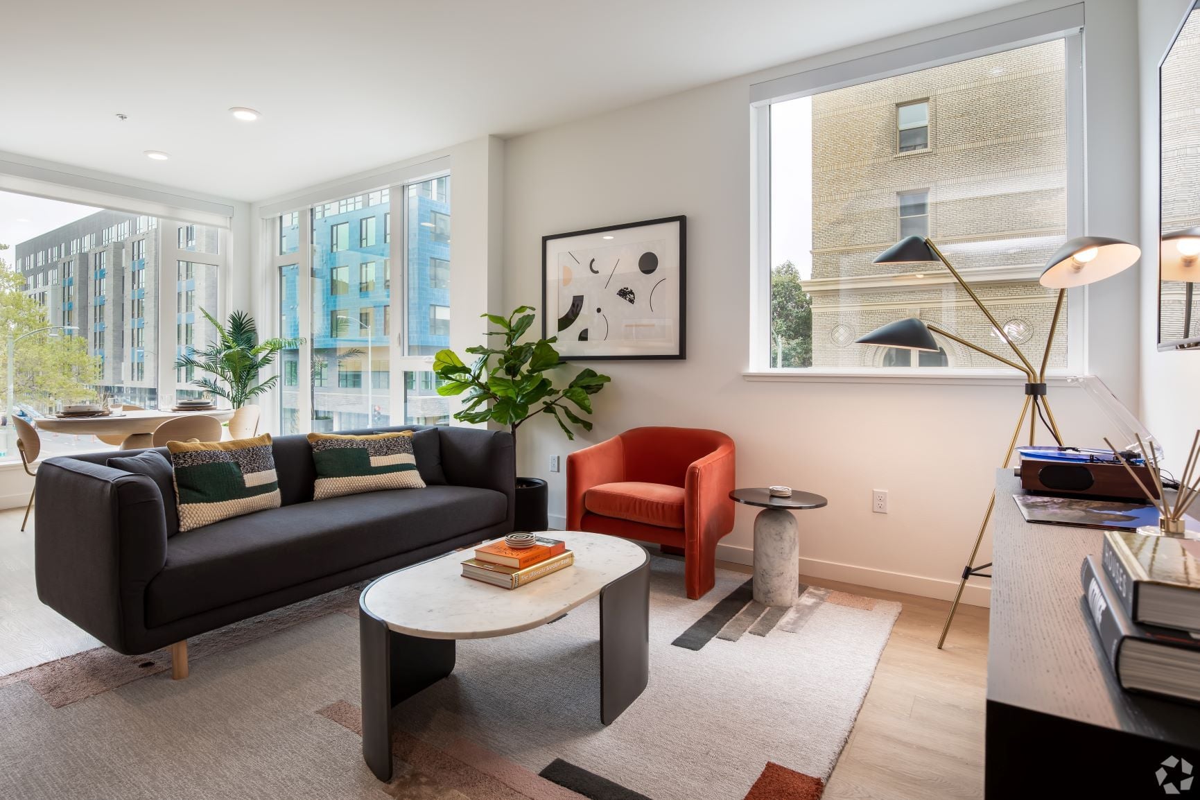 Living room with a dark grey sofa, red armchair, and a large window onto neighboring buildings
