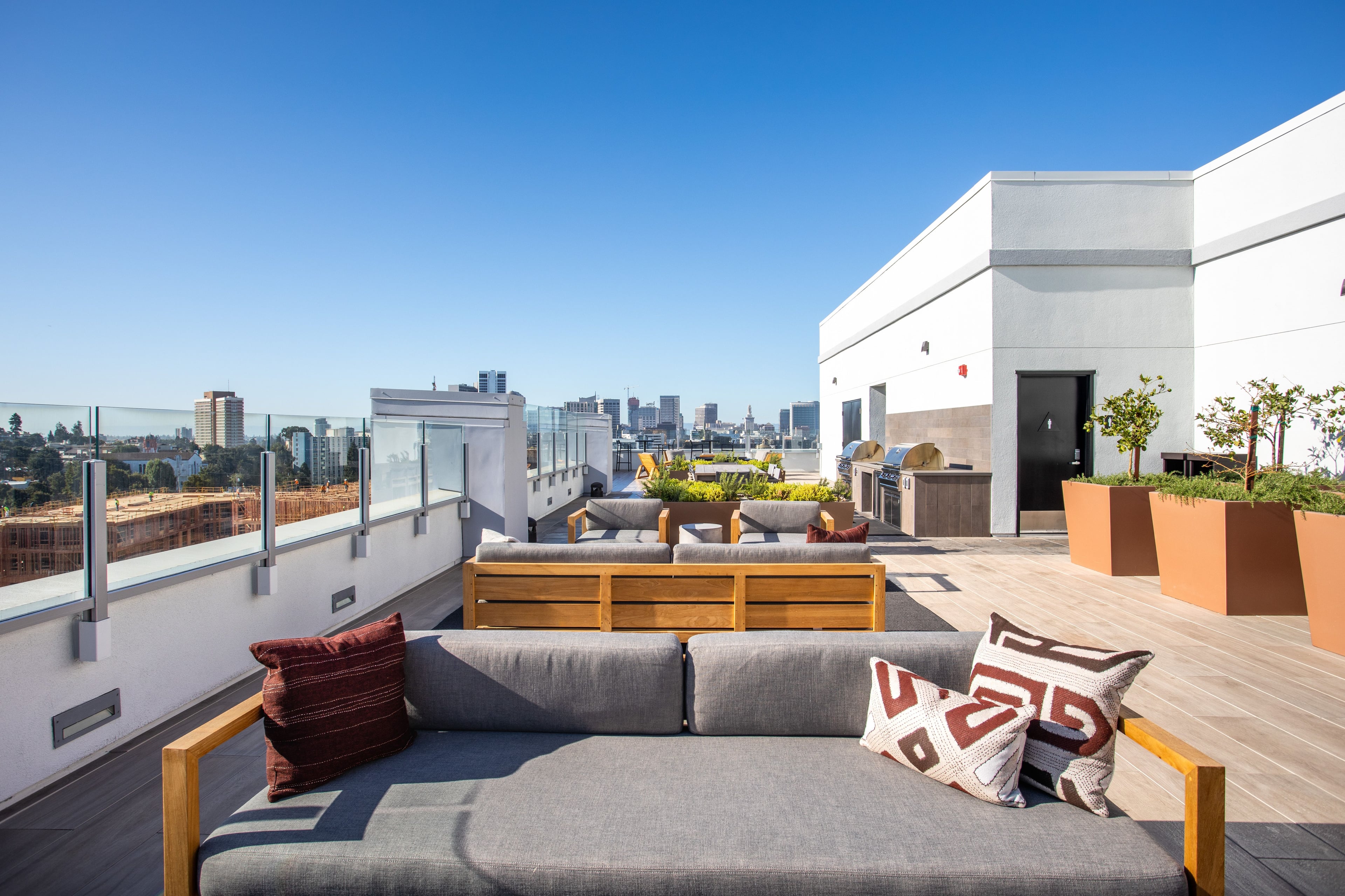 Rooftop lounge with a grey sectional and patterned pillows, downtown Oakland in the distance