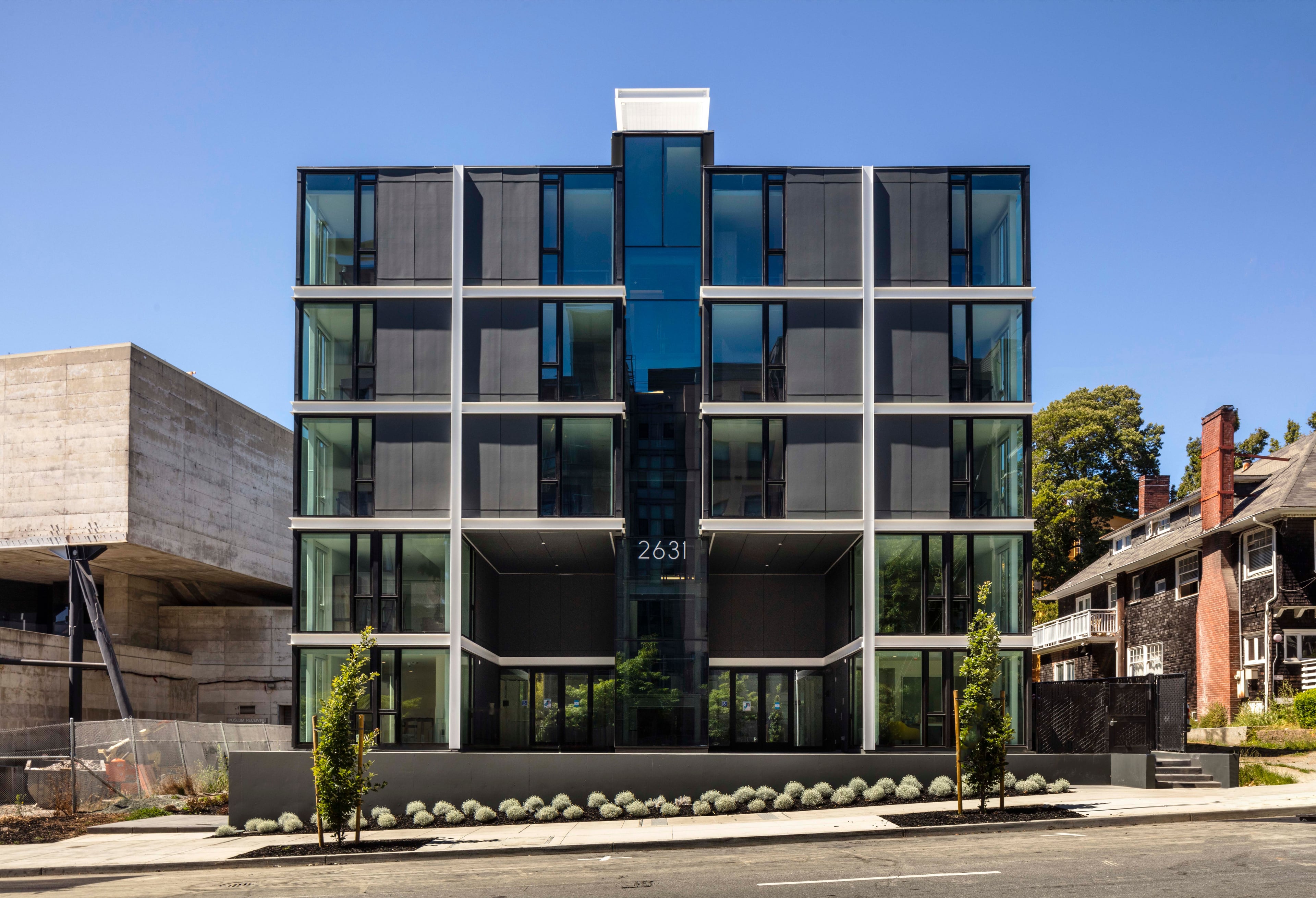 The Durant, a six-story building with a dark grid facade and glass, next to a concrete building and a brick house