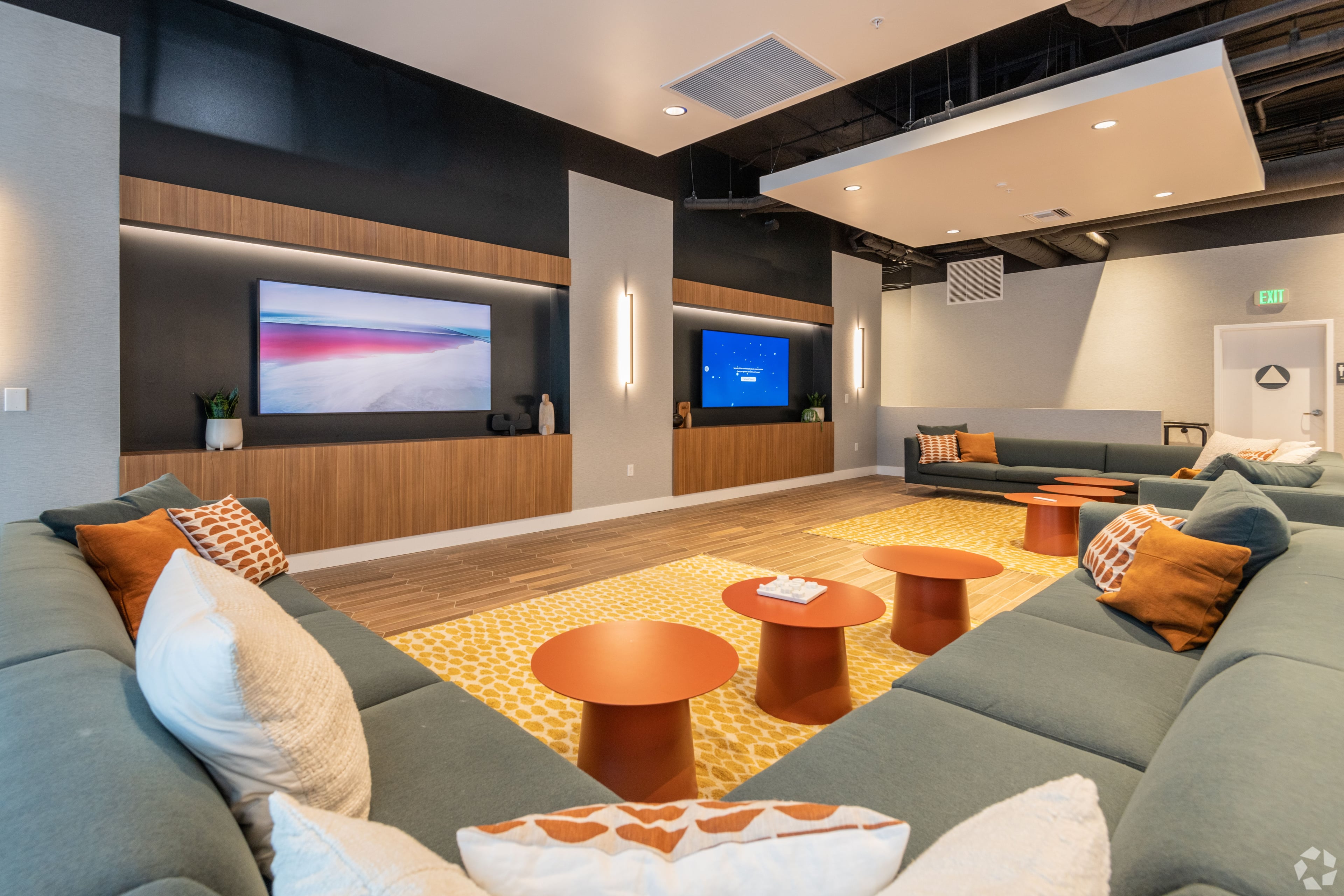 Sunken lounge with a wraparound sage sofa, orange side tables, and two TVs
