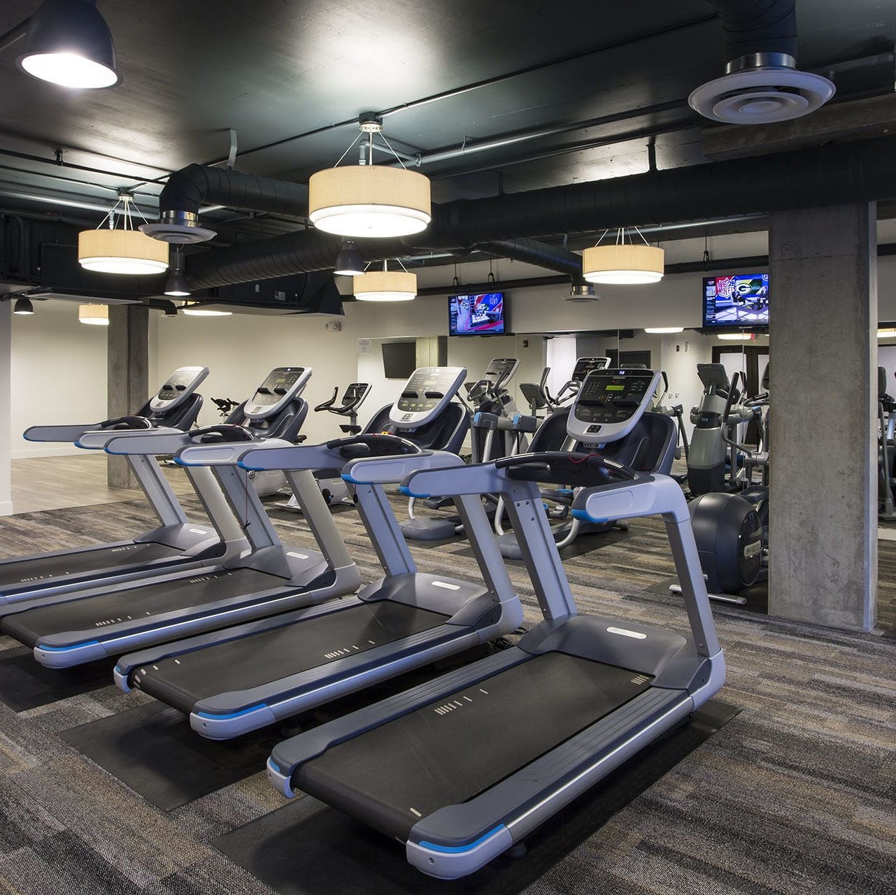 Fitness center with a row of treadmills, TVs, and round pendant lights