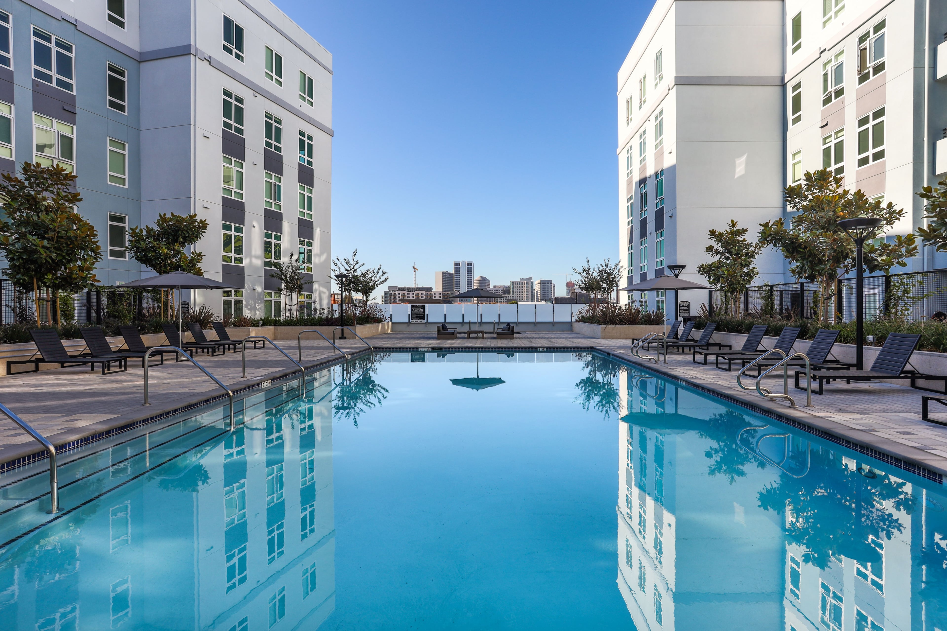 Rectangular pool on a deck with lounge chairs, the Oakland skyline visible past the buildings