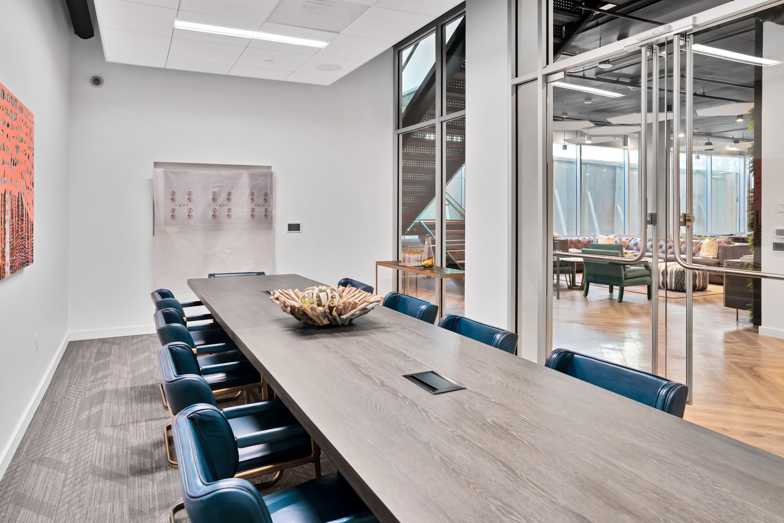 Conference room with a long dark table and navy chairs, glass wall to the lounge