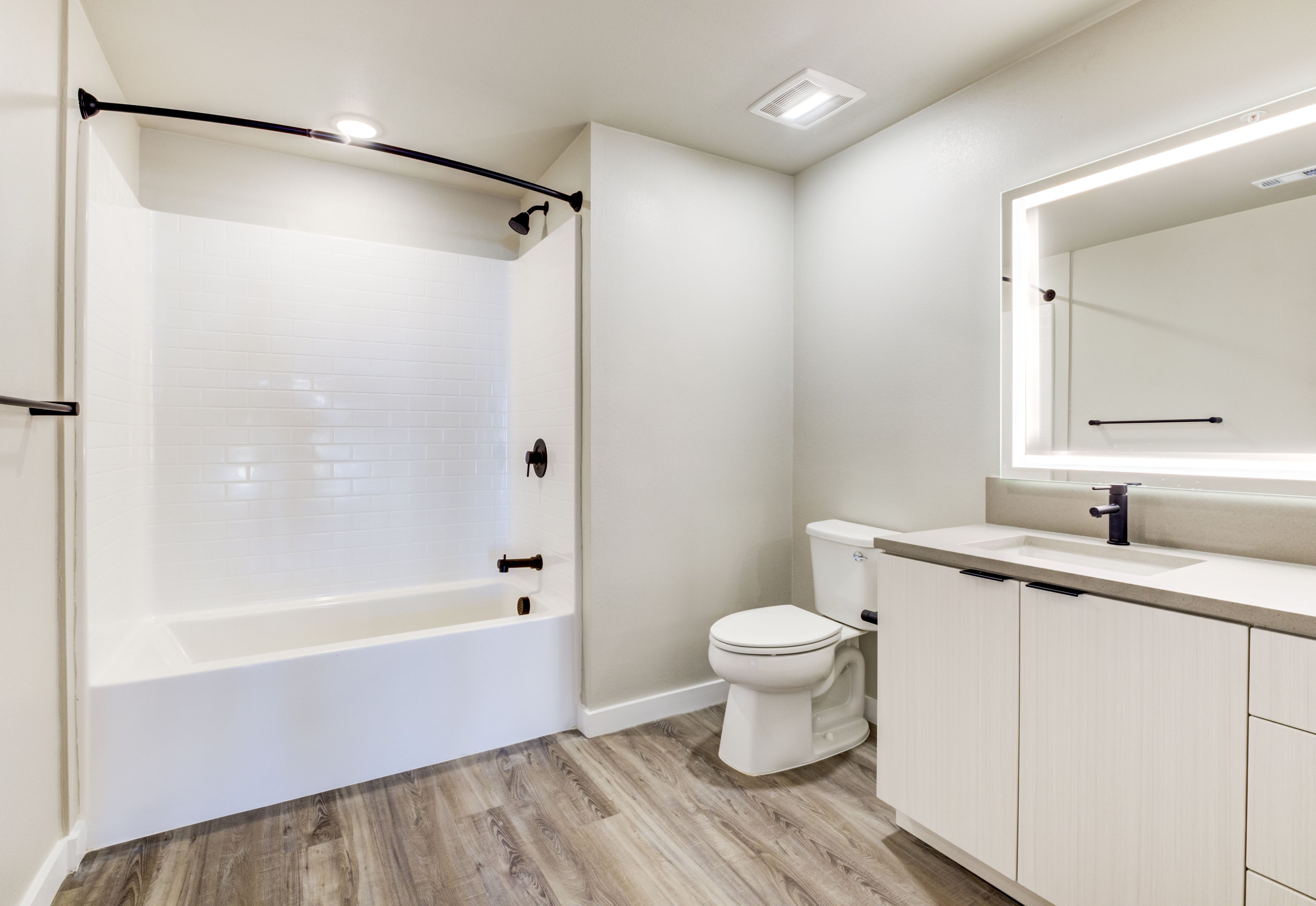 Bathroom with a white tub and shower, backlit mirror, and light wood vanity