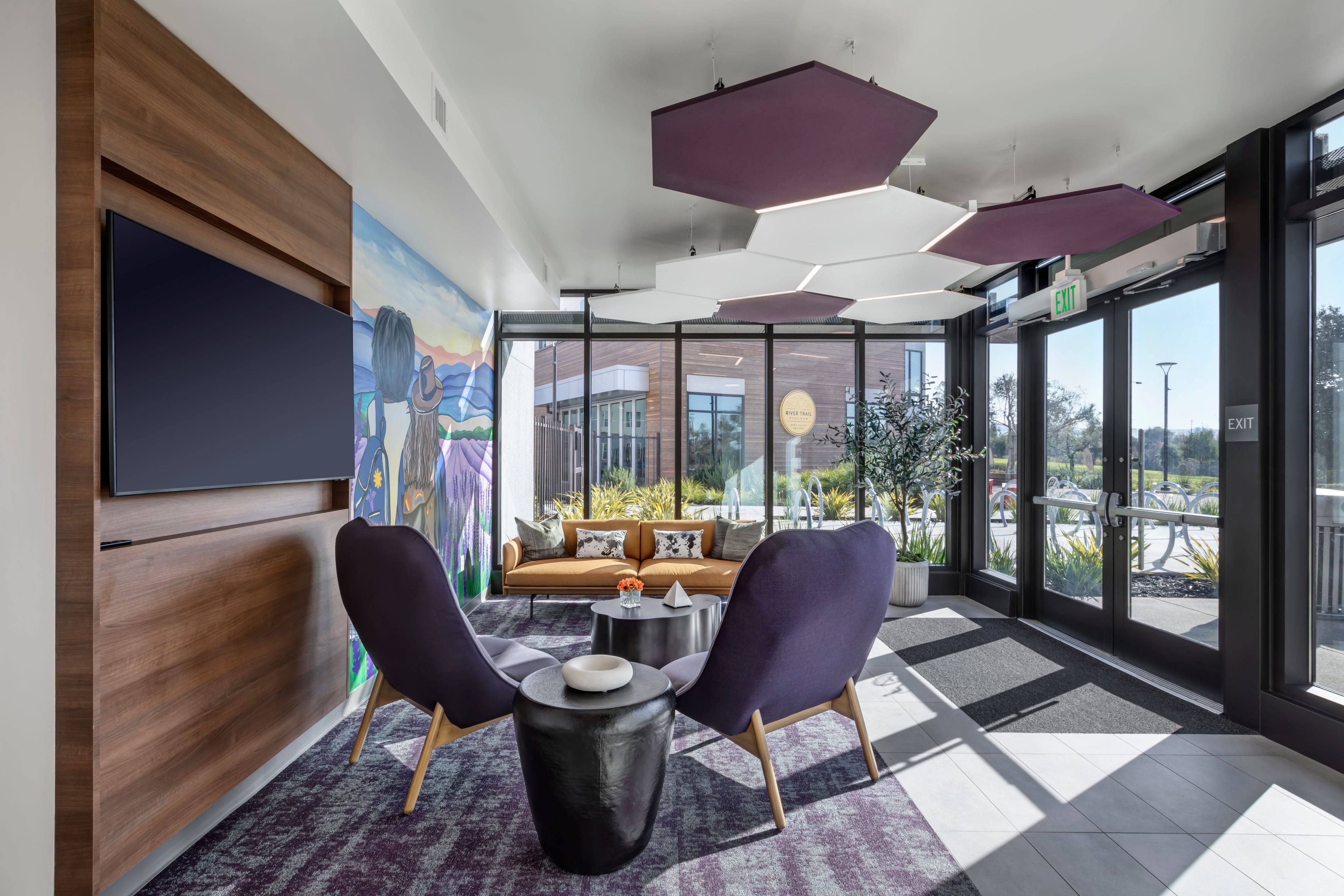 Lounge with purple armchairs, hexagonal ceiling panels, and a mural through the glass