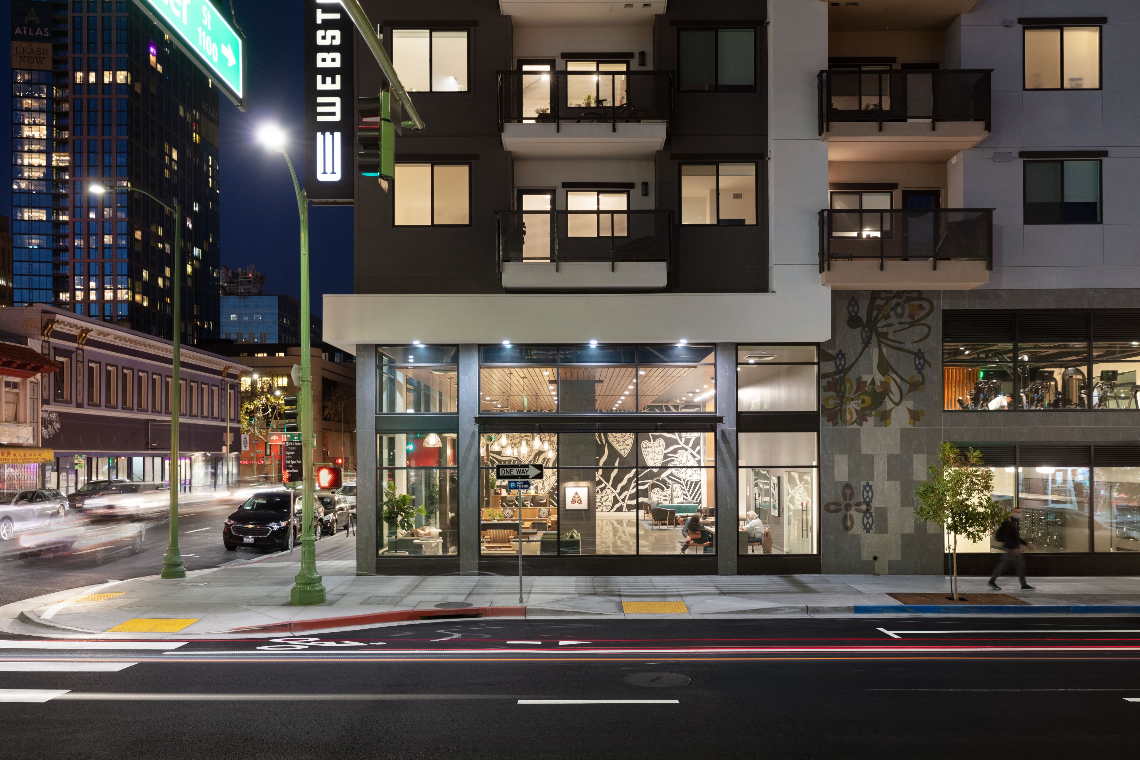 Corner entrance at night with lit lobby, the Webster Eleven sign above, and downtown towers behind