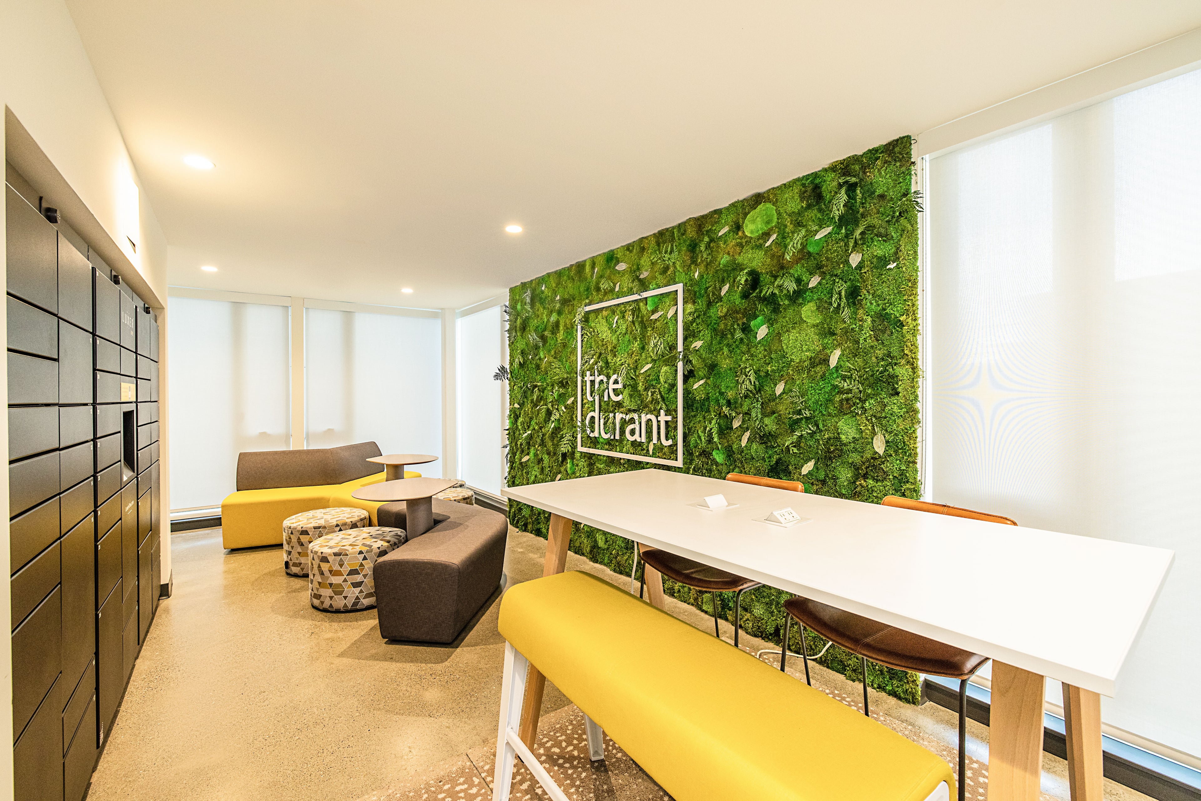 Lounge with a living green wall bearing “the durant” logo, yellow benches, and a white table