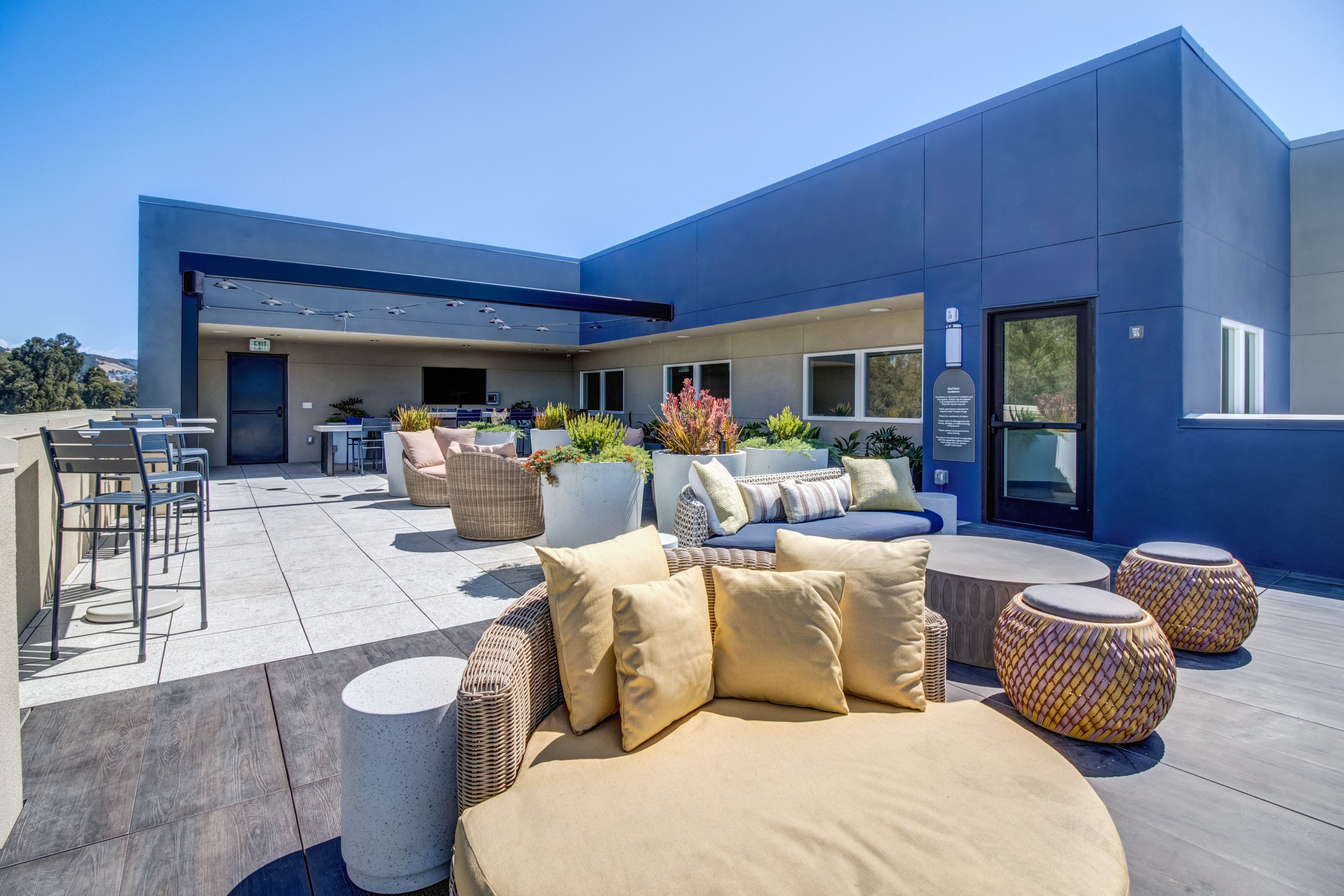 Rooftop deck with yellow cushioned seating, planters, and a covered lounge