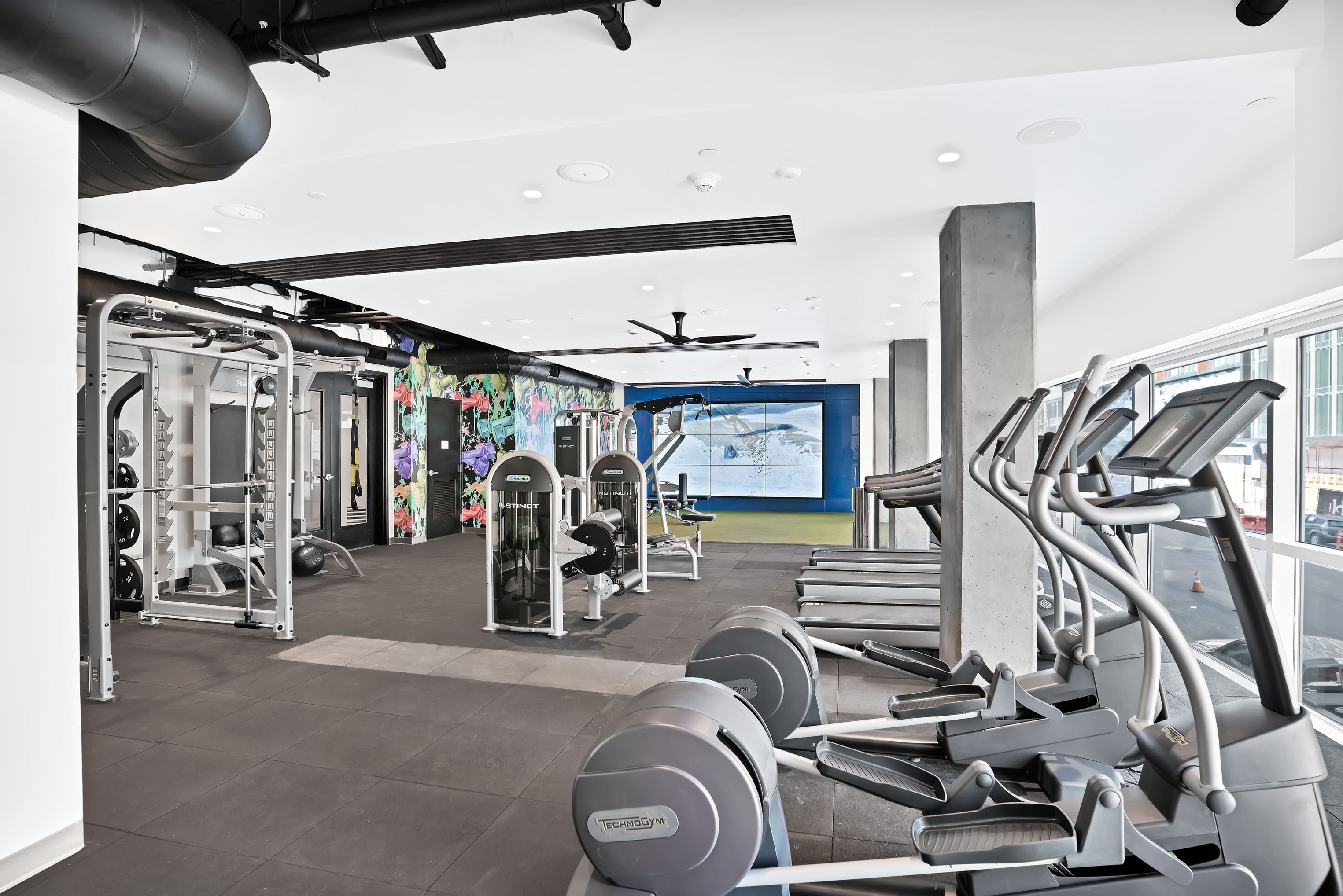 Fitness center with treadmills, ellipticals, and cable machines under exposed ceilings