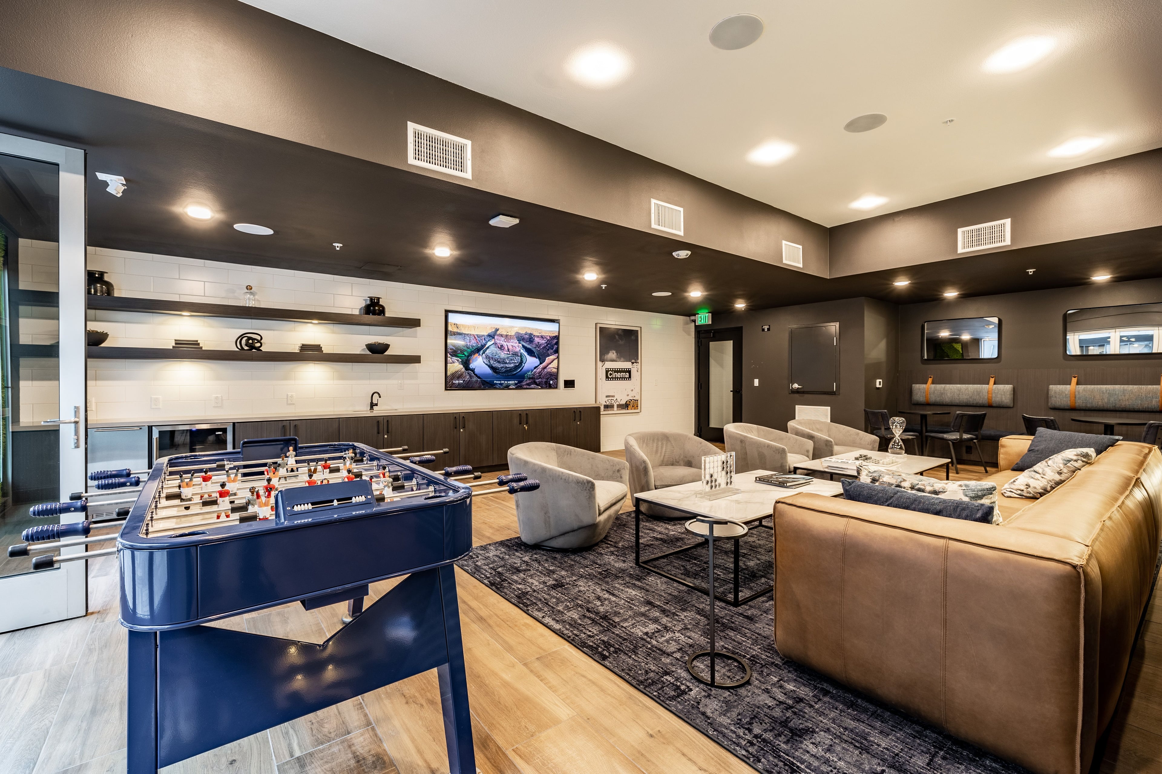Clubroom with a foosball table, brown leather sofa, and shelving around a TV