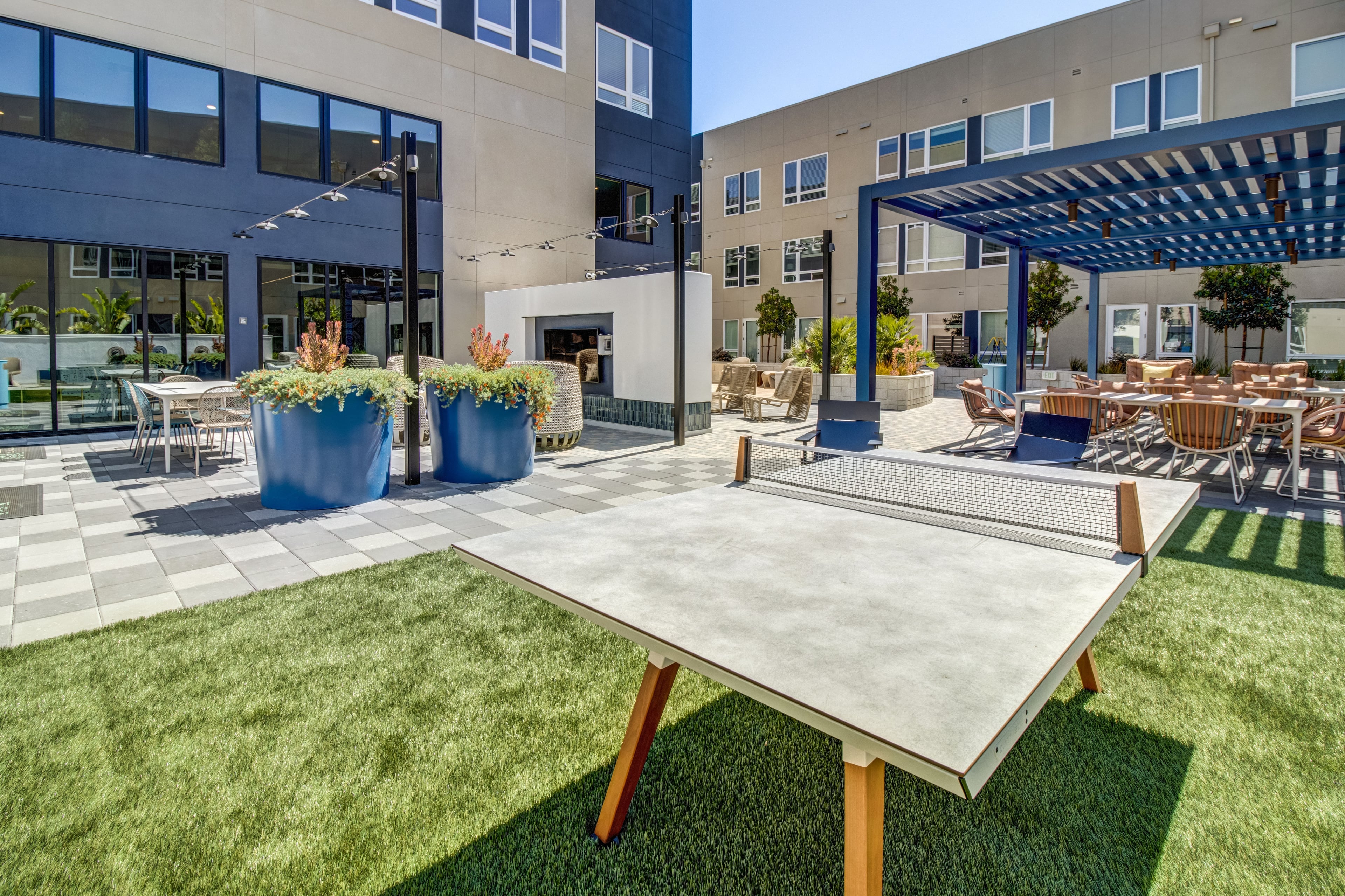 Courtyard with a concrete ping-pong table on turf, a pergola, and apartment windows behind